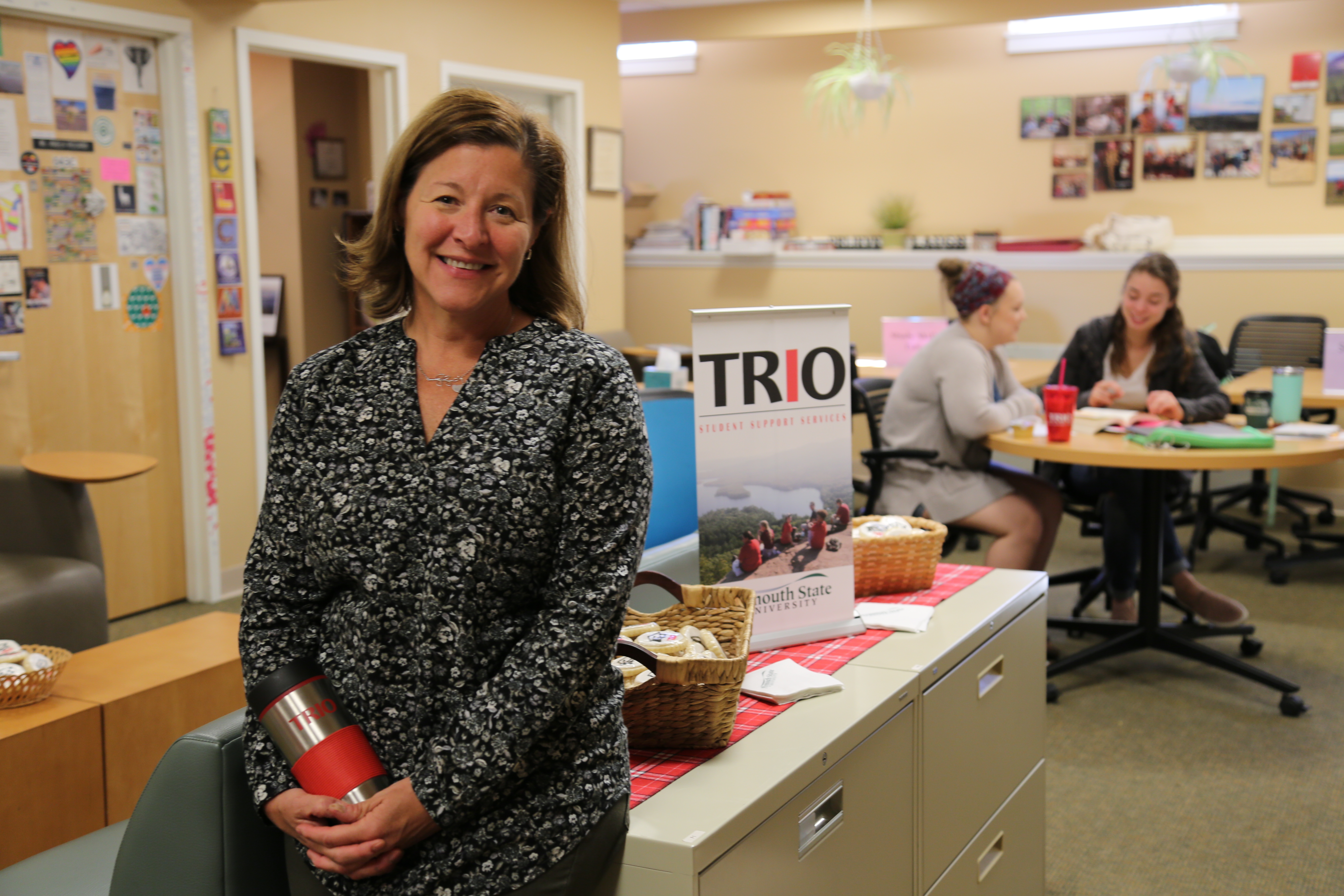 Woman with brown hair smiling in front of students working