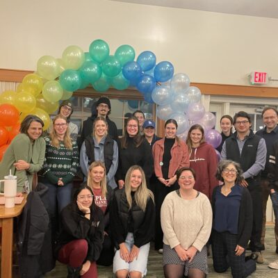 Senior seminar students gather at the party under a rainbow-colored balloon arch