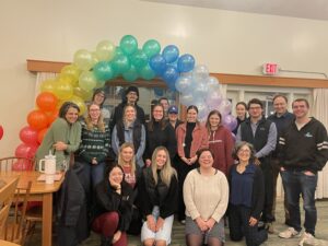 Senior seminar students gather at the party under a rainbow-colored balloon arch
