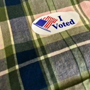 white and red heart "I voted" sticker on a flannel shirt